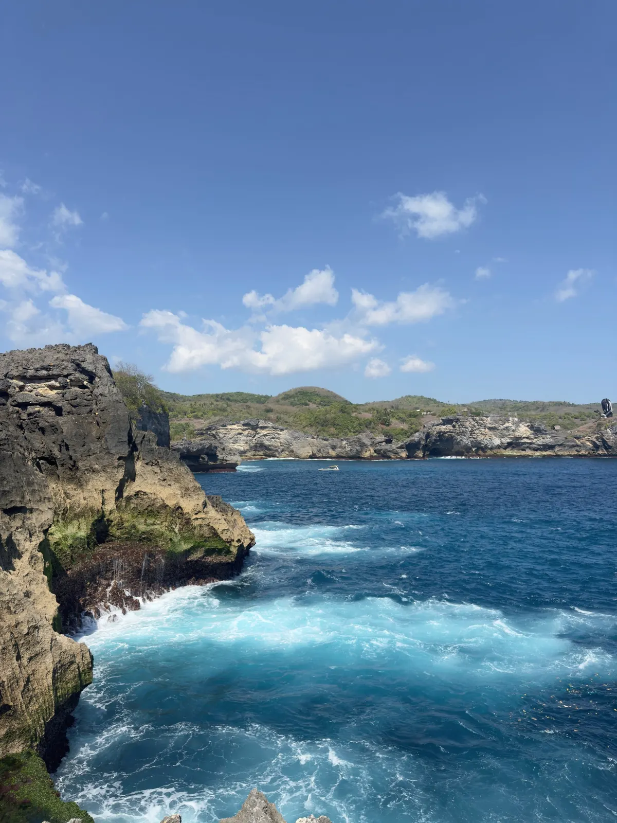 Limestone sea cliffs on Nusa Penida, deep blue water breaking white against the rocks under a bright sky.